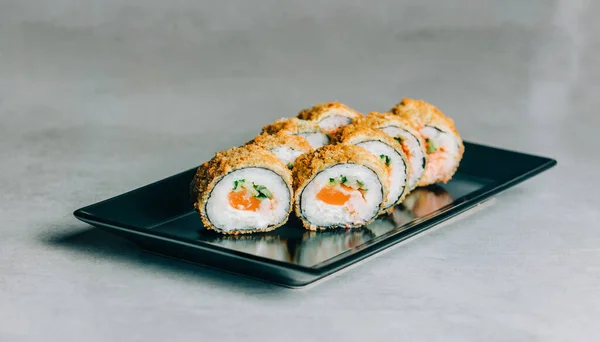 stock image Warm sushi rolls in dried breadcrumbs with salmon on black plate on gray background