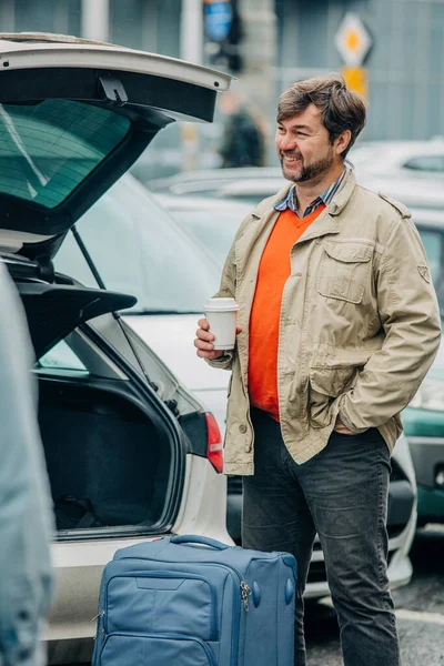 コーヒーと旅行バッグのカップを持つシニア男性は車の横に立つ ヴロツワフ ポーランド ストックフォト