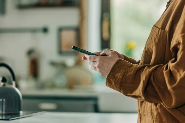 Mulher Camisa Marrom Segura Smartphone Mãos Cozinha Olhando Para Exibir — Fotografia de Stock