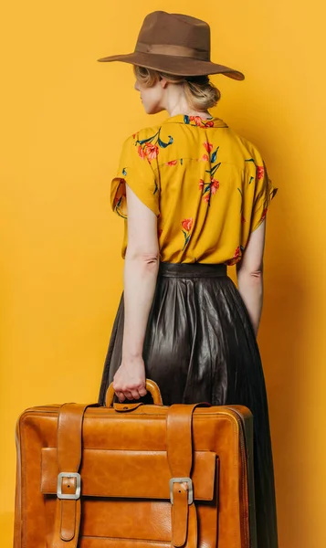 バックサイドビューでスタイリッシュなブロンド髪の女性で帽子とシャツとともにスーツケース上の黄色の背景 — ストック写真
