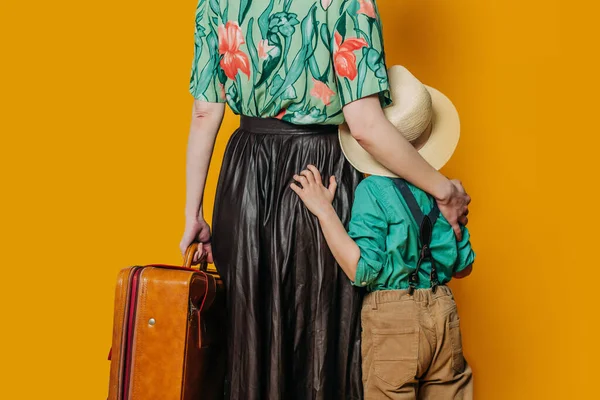 带着儿子和黄色背景手提箱的时髦女人的后视镜 免版税图库图片