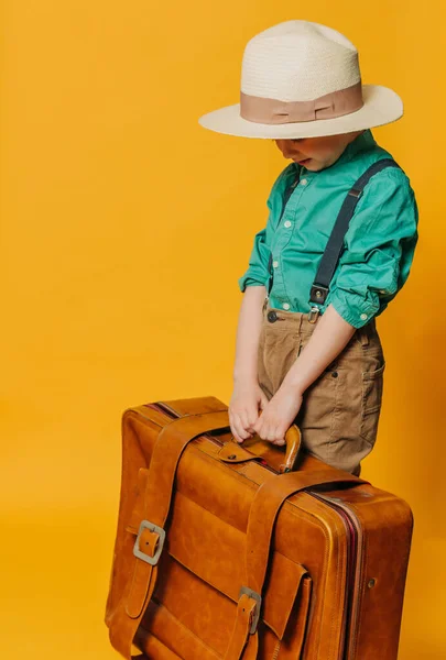 帽子の小さな男の子 黄色の背景にバッグ付きのサスペンダーと緑のシャツ ストックフォト