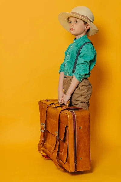 头戴帽子 身穿吊带衫 身穿绿色衬衫 背带黄色包袋的小男孩 图库照片
