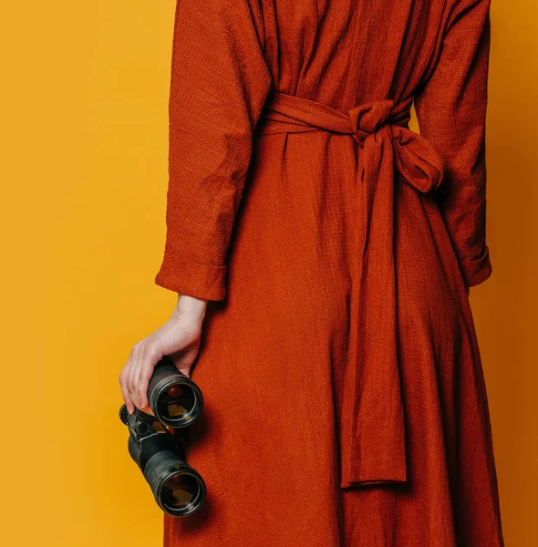 Mujer Con Estilo Vestido Marrón Con Binoculares Sobre Fondo Amarillo Imagen de archivo