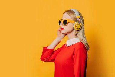 Sarı arka planda kulaklıkları olan kırmızı elbiseli şık sarışın kadın.