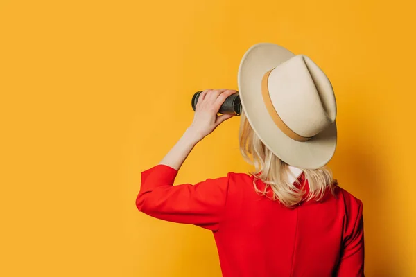 バックサイドビュー上の女性で帽子と赤ドレスとともに双眼鏡で黄色の背景 — ストック写真