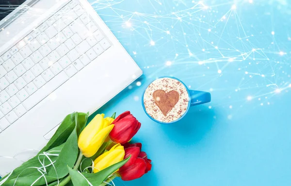 Cup of cappuccino with heart shape and computer with abstract connections , tulips on blue background.