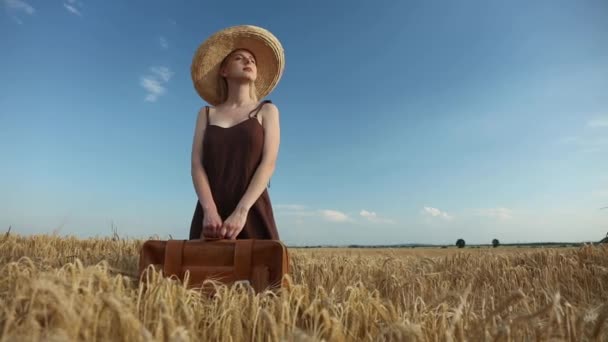 スタイリッシュなブロンド女性でドレスと帽子付きスーツケースで黄色小麦畑 — ストック動画