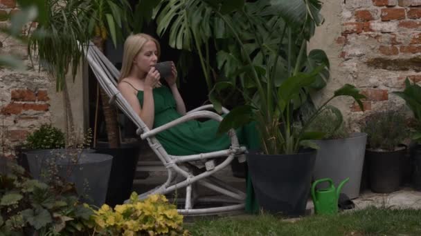緑のドレスの女性は 植物の周りに椅子に座って紅茶を飲む 夏の時間の季節 — ストック動画