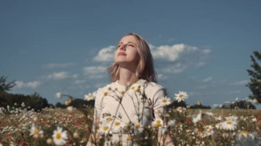 Beyaz elbiseli beyaz kadın yazın papatya çayırında ellerini kaldırır.