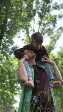 Havalı ve mutlu Avrupalı baba ve oğlu yazın açık havada omuzlarında, dikey video.