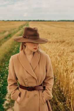 Kahverengi Vintage ceket ve buğday tarlasında şapka giyen Kafkas Sarışın Kadın