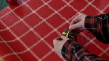  Masaya kırmızı kutular ve yeşil masa örtüsüyle Noel hediyelerini saran bir kadın.