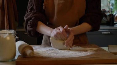 Önlüklü bir kadın evdeki mutfağında elle hamur yoğuruyor.