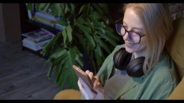 Orta yaşlı beyaz bir kadın, evinde bir koltukta oturmuş, sosyal medyada görüntüler izlerken gülüyor..