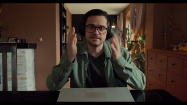 Yeşil tişörtlü orta yaşlı bir adam evdeki bilgisayar kamerasıyla online röportaj için arıyor. Masada oturuyor. Video görüntüleri var..