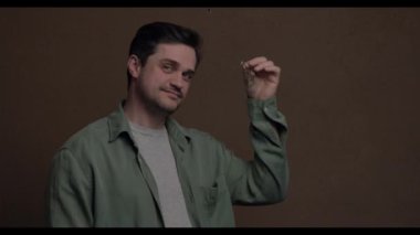 Beyaz bir adam elinde bir set emlak anahtarı ile kahverengi bir arka plan ve video görüntüsü tutuyor.