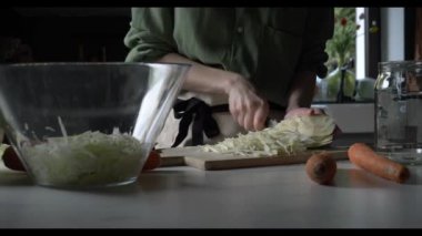 Önlüklü bir ev kadını evdeki mutfak masasında mayalanmak için lahana doğruyor..