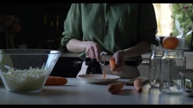 Evdeki mutfak masasında mayalanmak için havuç soyan önlüklü bir ev kadını..