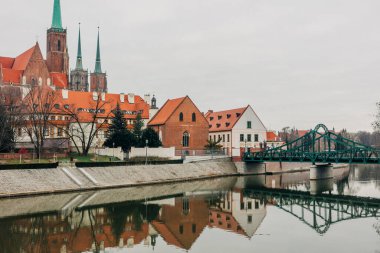 Polonya 'nın Wroclaw kentindeki Tumski Adası' nda nehir boyunca uzanan pitoresk bir köprüyle Gotik tarzı bir kilisenin çarpıcı manzarası.. 