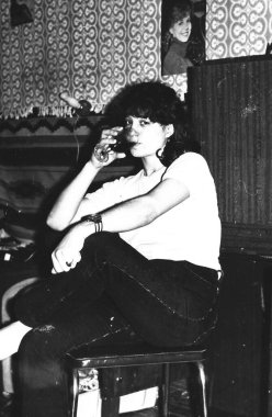 Genç bir kadının, bir koltukta oturmuş Sovyet yatakhanesinde komposto içerken çekilmiş siyah beyaz bir fotoğrafı.