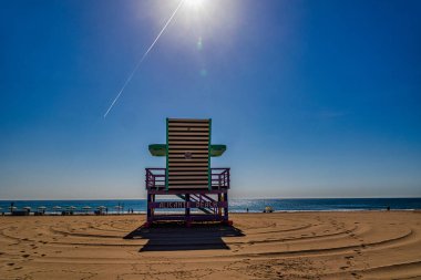 Parlak bir güneş boş bir sahilde cankurtaran sandalyesi üzerinde parlıyor.