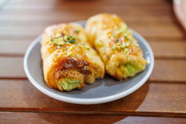 Yeşil kremayla dolu iki gevrek hamur işi gri bir tabakta oturur, üstleri kesilmiş fındıkla süslenir.