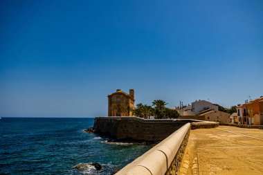 Sakin bir sahil geçidi taştan bir duvarın ve resimli binaların yanından geçiyor.