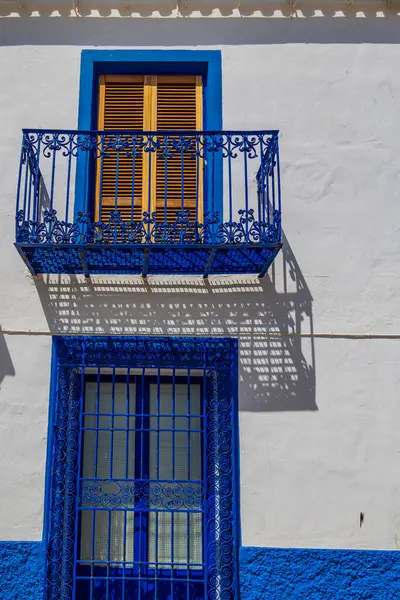 Parlak mavi işlenmiş demir bir balkon güneşli beyaz bir duvara karmaşık gölgeler bırakır..