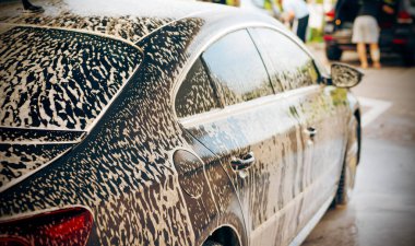 Gündüz vakti araba yıkamada koyu renk bir arabanın gövdesine beyaz köpük sürülür.