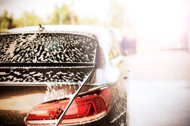 Güneşli bir havada araba yıkamada beyaz köpüklü bir arabanın arka görüntüsü.