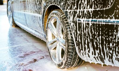 Gündüz vakti araba yıkamada koyu renk bir arabanın gövdesine beyaz köpük sürülür.