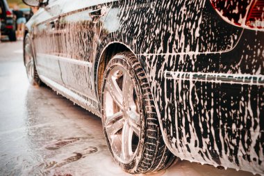 Gündüz vakti araba yıkamada koyu renk bir arabanın gövdesine beyaz köpük sürülür.