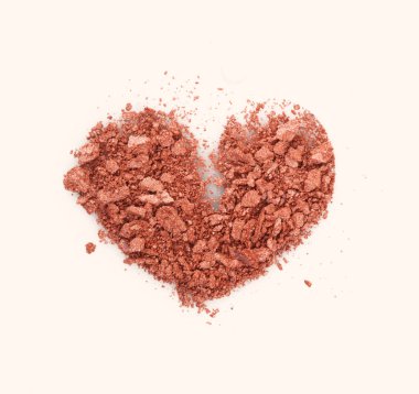 Paramparça ve ezilmiş inci bronz kalp şeklindeki göz farı, toz. Bej arka planda kırılmış kozmetik ürünleri. 