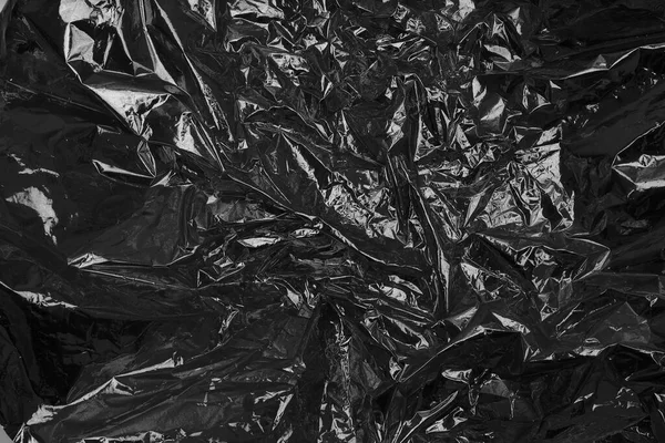 Black cellophane foil paper. Abstract glow texture copy space background.