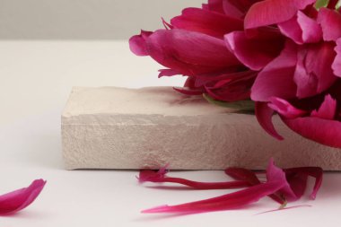 Purple pion flowert petal and stones platform podium on beige background. Minimal empty display product presentation scene. 