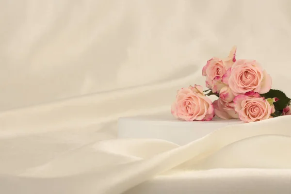 粉红玫瑰花束点缀在白色的讲台上和丝织品上浅浅的米色背景 最小空显示产品演示场景 — 图库照片