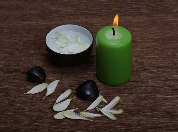 Brennende Grüne Kerze Schwarze Steine Und Blütenblätter Auf Braunem Holzmattenhintergrund — Stockfoto