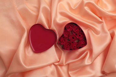 Kalp çerçeveli hediye paketi ve gül çiçekleri. Soyut bej rengi, pembe inci dalga, ipek kumaş dokusu arkaplanı.