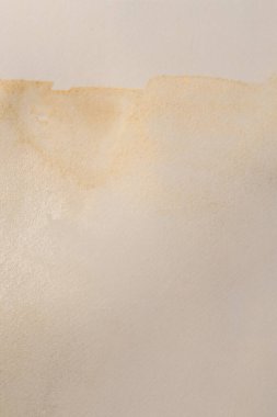 Gold glitter watercolor grain blot on beige paper texture background.	