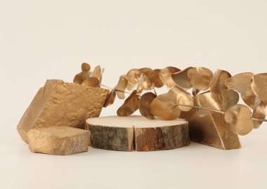 Taşlar, ahşap daire disk platform podyumu ve bej arka planda altın yaprak dalı. En az boş ürün sunum sahnesi.