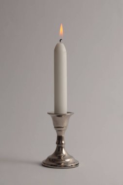 Gümüş şamdanda tek başına mum yakmak. İyi akşamlar, gece aydınlığı ve gölge grisi tarafsız arka plan. Minimalist hareketsiz hayat.