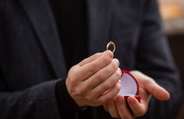 Bir adam elinde kırmızı kurdeleyle yüzük veriyor.