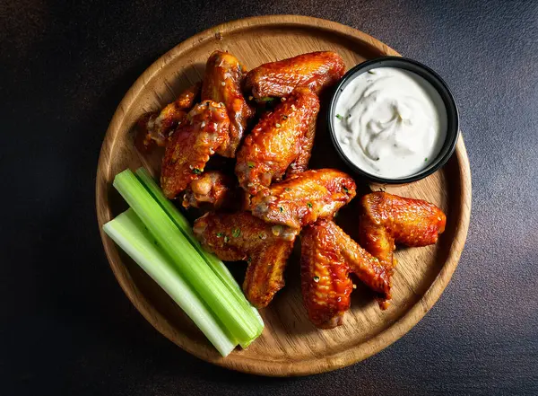 Soslu kızarmış tavuk kanadı ve koyu bir arka planda bira.