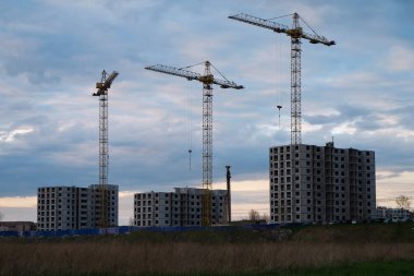Unfinished high-rise buildings and construction cranes next to them. Beautiful sunset clouds on the background