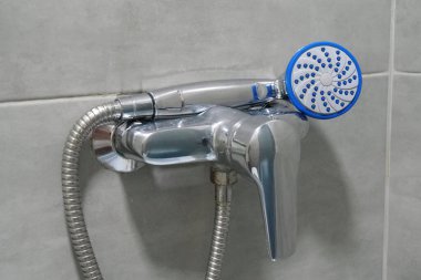 Shower head in bathroom, chrome faucet and grey tiles on the walls, water is not flows