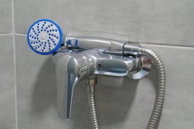 Shower head in bathroom, chrome faucet and grey tiles on the walls, water is not flows