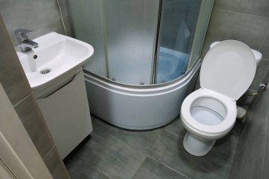 Toilet room interior with white toilet bowl, shower cabin and grey wall tiles