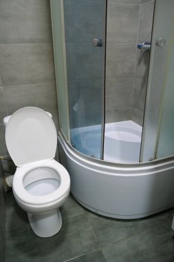 Toilet room interior with white toilet bowl, shower cabin and grey wall tiles