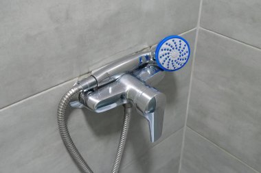 Shower head in bathroom, chrome faucet and grey tiles on the walls, water is not flows
